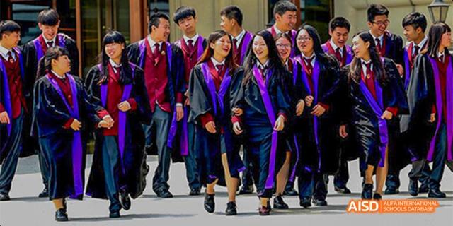 A group of students from Beijing Aidi School in red uniforms and graduation robes walking together.