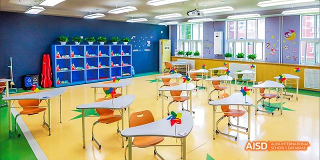 A bright, empty classroom at Beijing Aidi School with orange tables and chairs.