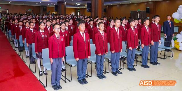 A line of students from Beijing Aidi School in red uniforms standing neatly in a corridor.