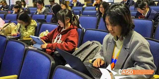 A student from Beijing Aidi School with a laptop, seated in an auditorium.