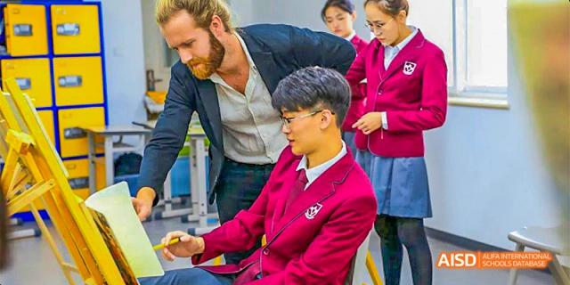 A teacher assisting a male student from Beijing Aidi School in a red jacket with his work on a computer.