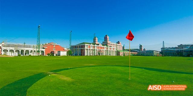 The main academic building of Beijing Aidi School, a red and white structure with a large grassy field in front of it under a clear blue sky