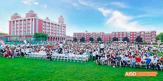 A large crowd of students gathered for an outdoor event in front of the Beijing Aidi School campus buildings