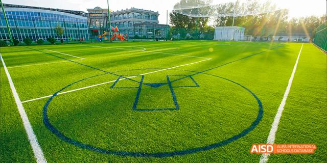 An empty artificial turf sports field at Beijing Aidi School, with soccer goalposts and field markings visible.