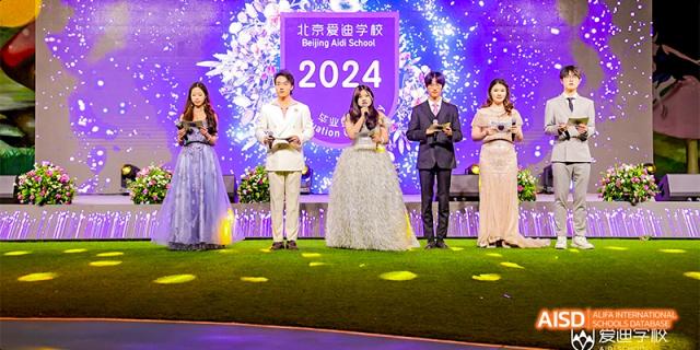 A woman in a white dress and a man in a white suit standing on a stage during an event at Beijing Aidi School.
