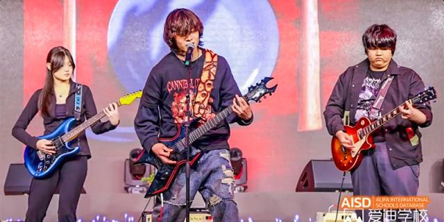 A male student from Beijing Aidi School playing an electric guitar on a stage during a performance.