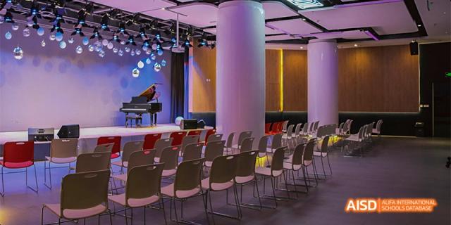An empty auditorium at Beijing Aidi School with rows of chairs facing a stage with a piano.