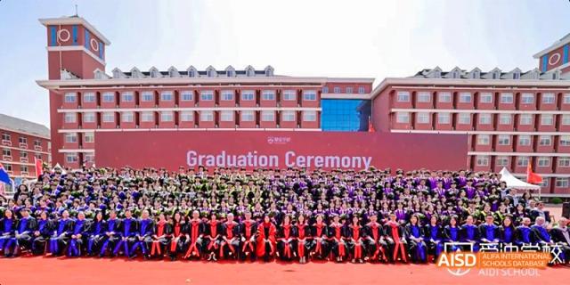 A large group of Beijing Aidi School students and staff posing for a group photo on a field during a graduation ceremony.