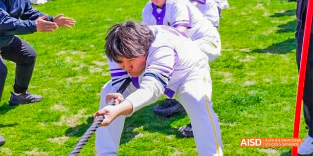 Two students from Beijing Aidi School participating in a tug-of-war game on a grassy field.
