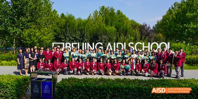 A large group of students from Beijing Aidi School in red uniforms posing for a photo outdoors.