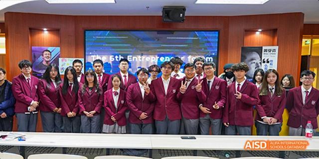 A group of students from Beijing Aidi School in maroon jackets posing indoors with a presentation screen in the background.