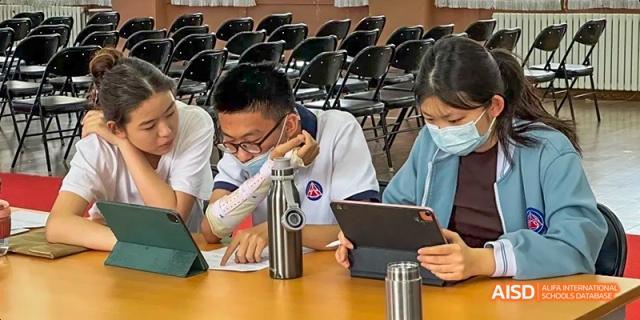 A Beijing No.8 High School student focuses intently on a tablet, with a water bottle on the desk, in a classroom setting.