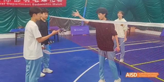 Two Beijing No.8 High School students playing or preparing to play badminton on an indoor court.