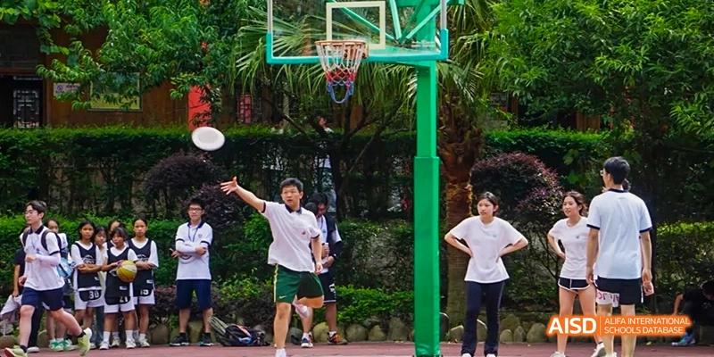 A Beijing No.8 High School student raising their arms under a basketball hoop on an outdoor court, with other students in the background.