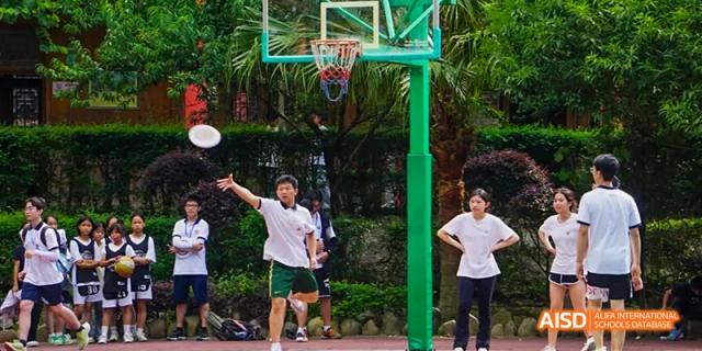 A Beijing No.8 High School student raising their arms under a basketball hoop on an outdoor court, with other students in the background.