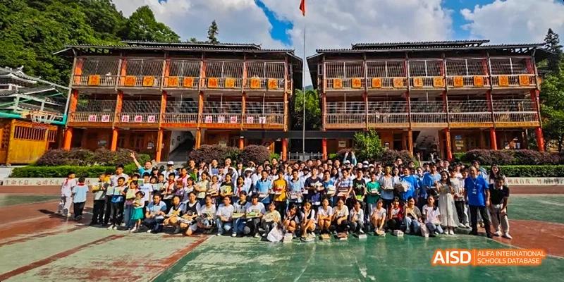 A large group of Beijing No.8 High School students and staff posing for a group photo outdoors in front of a traditional-style school building with a red flag flying.