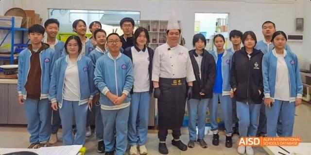 A group of Beijing No.8 High School students posing with a chef in a white uniform in a kitchen or classroom.