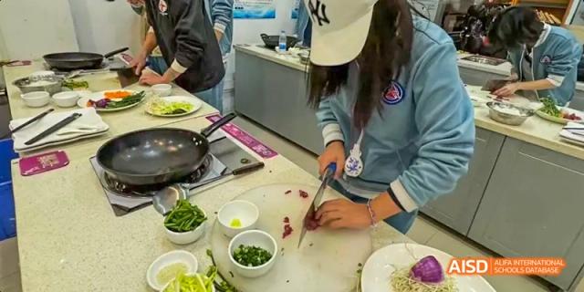A female Beijing No.8 High School student, wearing a baseball cap, uses a knife to chop ingredients during a culinary class.