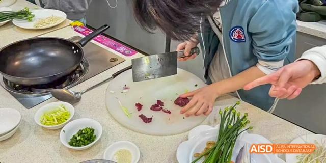 A Beijing No.8 High School student cutting meat on a white cutting board during a cooking lesson.