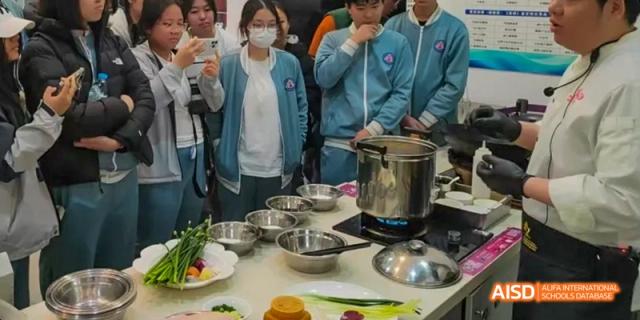 A group of Beijing No.8 High School students observe and gather around a cooking station with bowls and a small stove.