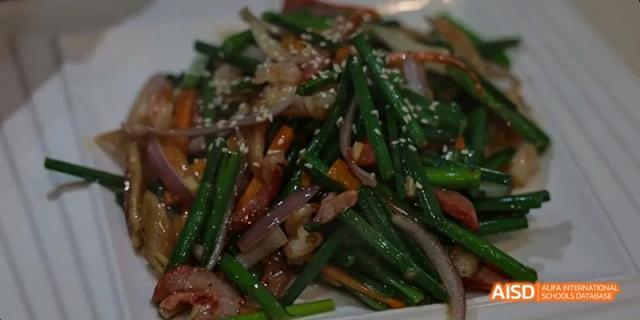 A close-up of a stir-fried dish with green onions and dark sauce, prepared by a Beijing No.8 High School class.