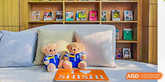 A teddy bear wearing a Chengdu Shishi High School Beihu Campus AP Curriculum uniform sits next to a pillow with the school's logo.