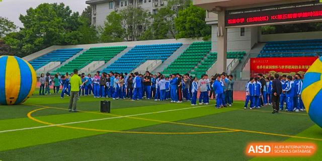 Chengdu Shishi High School Beihu Campus AP Curriculum students in blue uniforms are seated in the stands on a sports field.