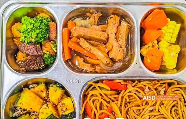 A meal tray with multiple compartments containing different dishes like noodles, vegetables, and chicken at Chongqing Depu Foreign Language School