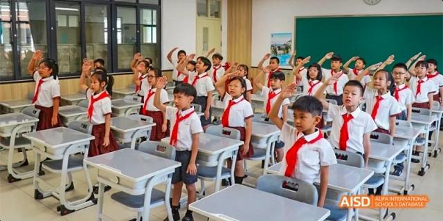 A bright classroom full of young students, likely in an elementary grade, smiling and raising their hands at DongGuan Laguna Verona Foreign Language School.