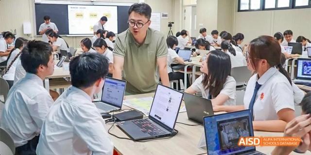 A male teacher working closely with two students on laptops during a lesson in a modern classroom or study space at DongGuan Laguna Verona Foreign Language School.