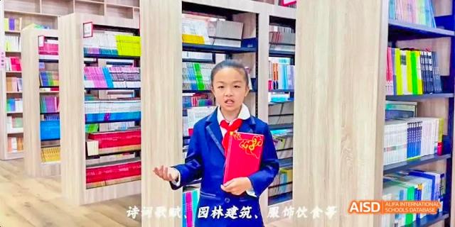 A young student in a blue suit holding a red certificate or award while standing in a classroom or library at DongGuan Laguna Verona Foreign Language School.