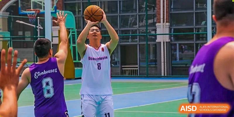 Male basketball player in a white and red jersey taking a shot on a court at DongGuan Laguna Verona Foreign Language School.