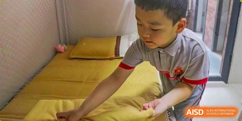 A young boy making a yellow-sheeted bed in a dormitory room, possibly at DongGuan Laguna Verona Foreign Language School.