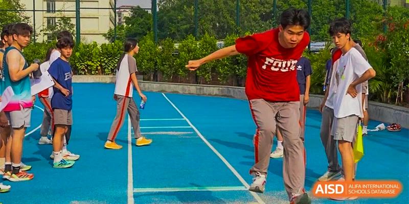 A male student in a red shirt jumping or participating in a track and field activity on a blue surface at DongGuan Laguna Verona Foreign Language School.