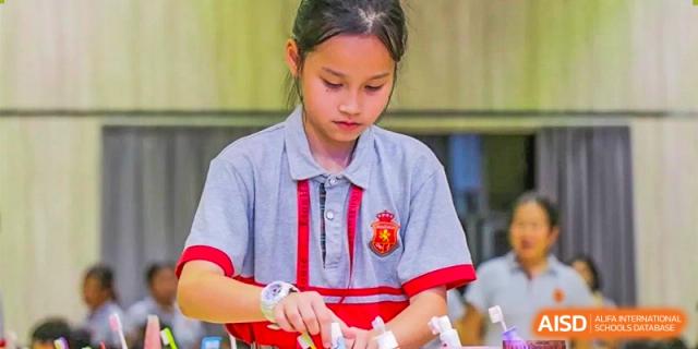 A female student in a gray and red school uniform focusing on an activity or craft project at DongGuan Laguna Verona Foreign Language School.