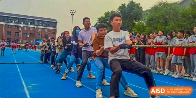 A group of male students pulling a rope in a tug-of-war competition on a blue sports surface at DongGuan Laguna Verona Foreign Language School.