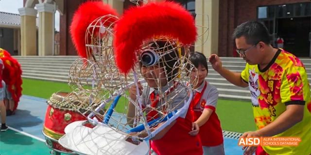 A student wearing a red, spiky Roman helmet playing a sports game with a racquet and net, possibly during a school field day at DongGuan Laguna Verona Foreign Language School.