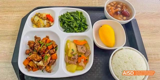 A balanced school lunch tray featuring steamed vegetables, stir-fried dishes, and a piece of mango for dessert at DongGuan Laguna Verona Foreign Language School.