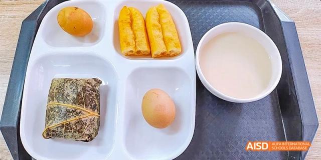 A school cafeteria tray with three spring rolls, a small bread roll, and a peeled egg at DongGuan Laguna Verona Foreign Language School.