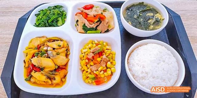 A colorful school lunch tray with mussels, corn, chopped peppers, a bowl of rice, and seaweed soup at DongGuan Laguna Verona Foreign Language School.