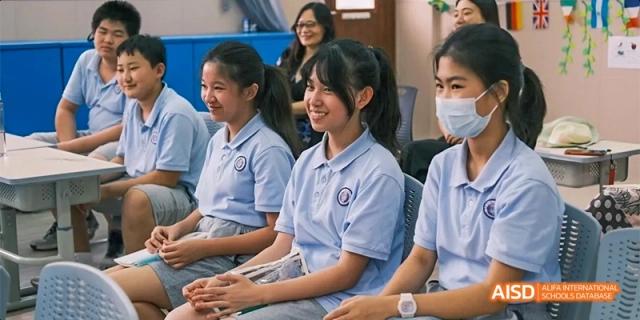 A group of female students wearing light blue school uniforms, seated and smiling during a class or assembly at GDUFS International School Guangzhou.