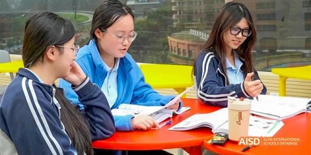 A female student wearing glasses, reviewing materials and engaging in a discussion with classmates at a table at GDUFS International School Guangzhou.
