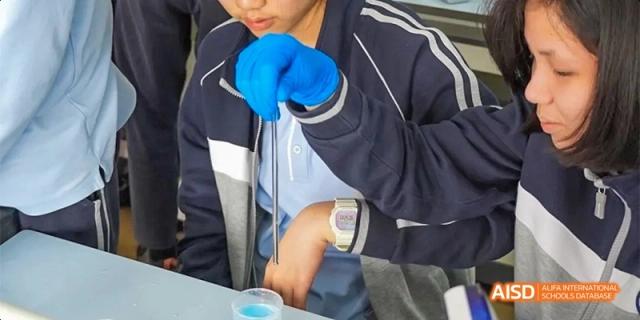 A student in gloves and safety glasses carefully using a pipette or syringe for an experiment in the science lab at GDUFS International School Guangzhou.