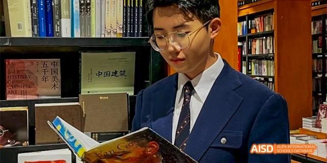 A male student in a suit and tie sitting and reading a book in the library at GDUFS International School Guangzhou.