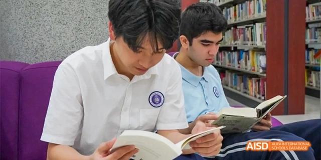 Two male students in school uniforms sitting in the library and reading a textbook or other material together at GDUFS International School Guangzhou.
