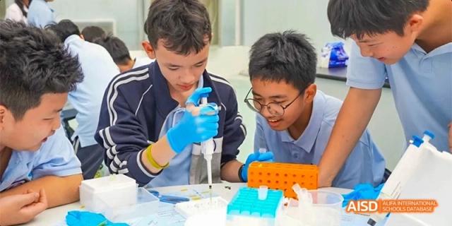 Students wearing gloves and safety glasses, collaborating on a practical science experiment or technical project at GDUFS International School Guangzhou.