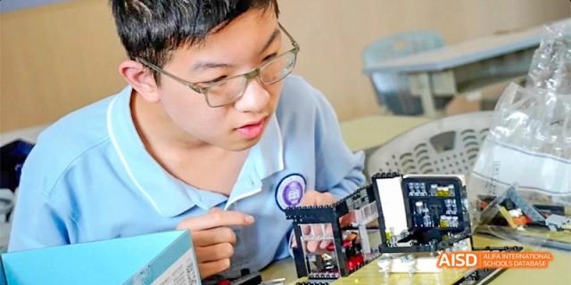 A male student in a blue shirt pointing to or interacting with content on a mobile phone or tablet at GDUFS International School Guangzhou.