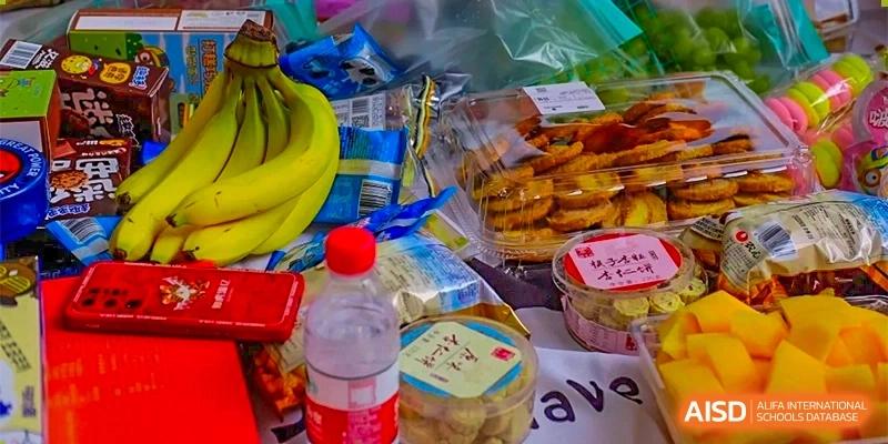 A close-up of a table with baked goods, bananas, and drinks set up for a school fair or market stall at GDUFS International School Guangzhou.
