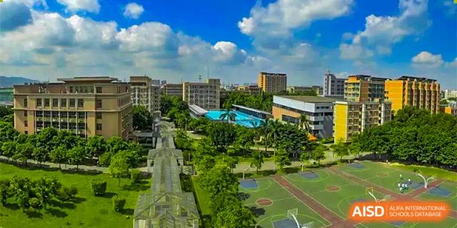 An aerial view of a lush green school campus, showing sports fields, trees, and tall school buildings under a blue sky at GDUFS International School Guangzhou.