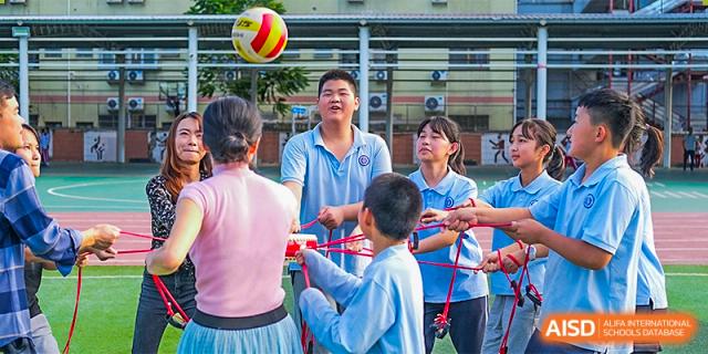 Students and a teacher playing a team-building game with ropes and a ball outdoors on the school grounds at GDUFS International School Guangzhou.